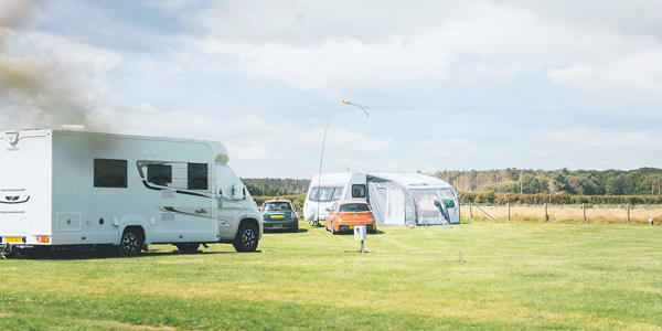 Two touring vans and cars parked on touring pitches at a UK holiday park with green grass and a blue sky above 