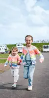 Children holding hands and running past caravans