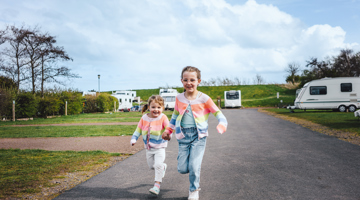 Children holding hands and running past caravans